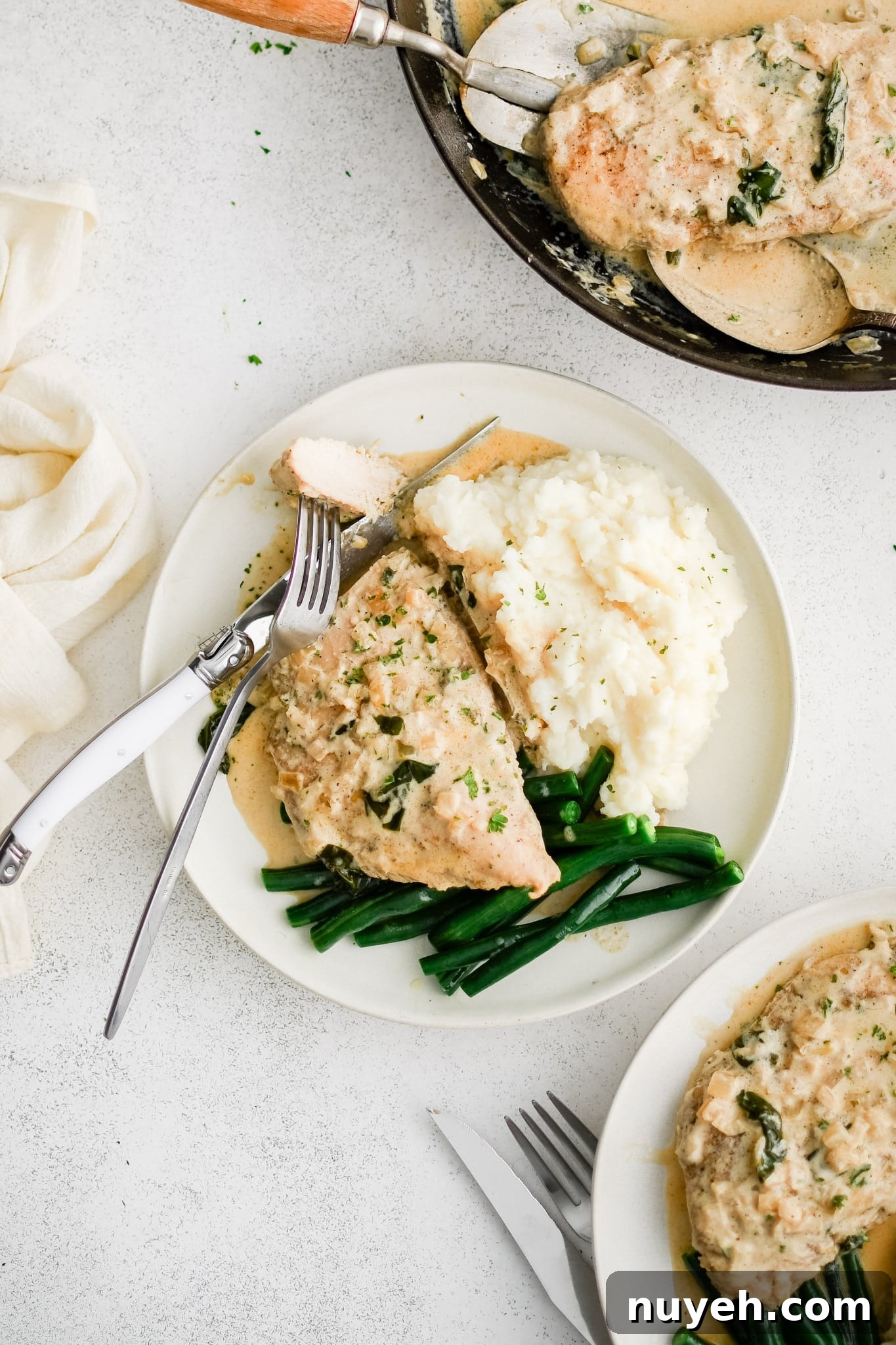 Three white serving plate filled with one piece of cooked chicken, a scoop of mashed potatoes, and pan-fried green beans all smothered in creamy boursin cheese sauce.