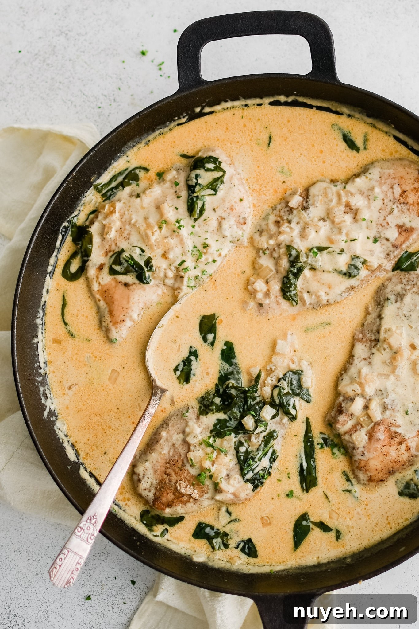 Well-seasoned and cooked chicken cutlets nestled into a large cast-iron skillet filled with simmering boursin cheese sauce with spinach and onions.