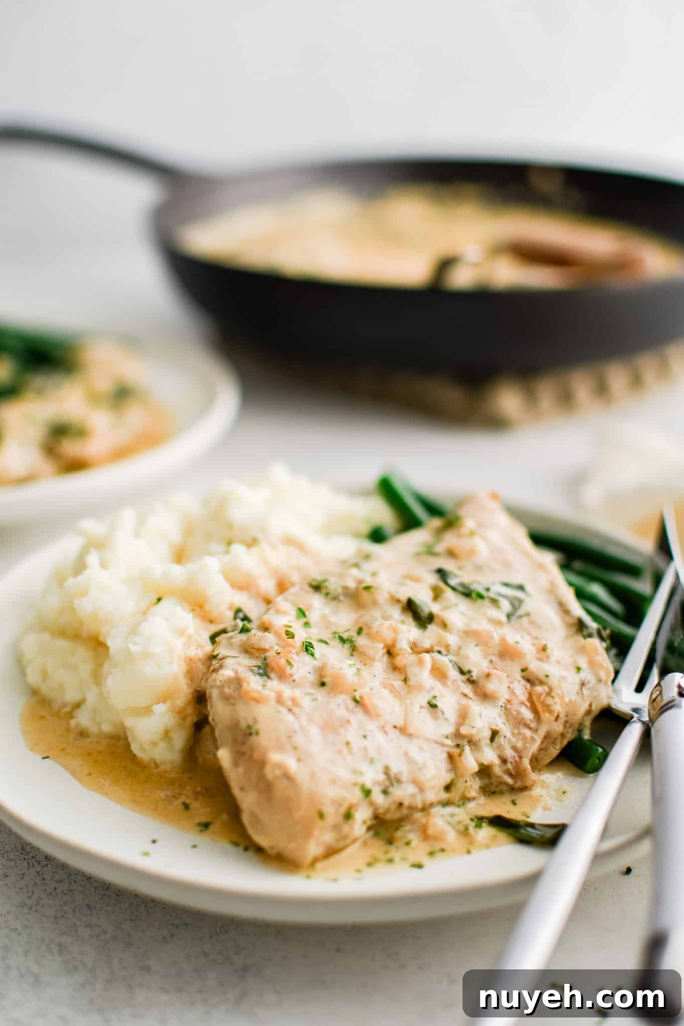 White serving plate filled with one piece of cooked chicken, a scoop of mashed potatoes, and pan-fried green beans all smothered in creamy boursin cheese sauce.