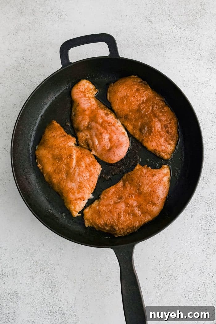 Four chicken cutlets seasoned all over with olive oil, salt, black pepper, garlic powder, onion powder, and paprika cooking in a large cast-iron skillet.