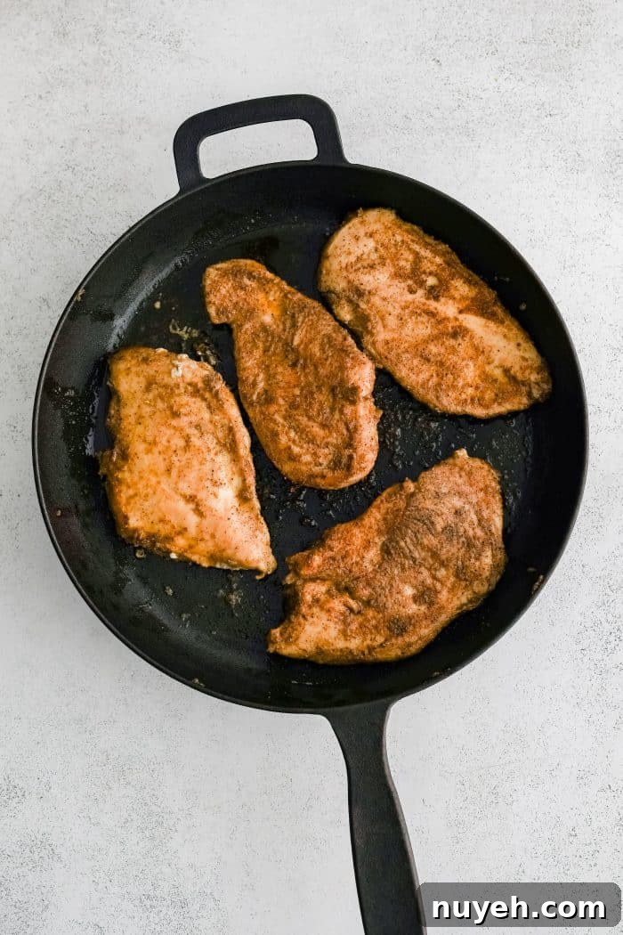 Four fully cooked chicken cutlets seasoned all over with olive oil, salt, black pepper, garlic powder, onion powder in a large cast-iron skillet.