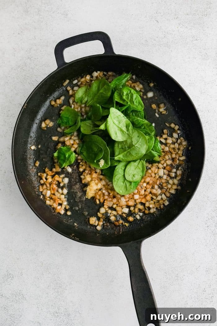 Large cast iron skillet filled with sauteing golden softened onions and a handful of fresh spinach.