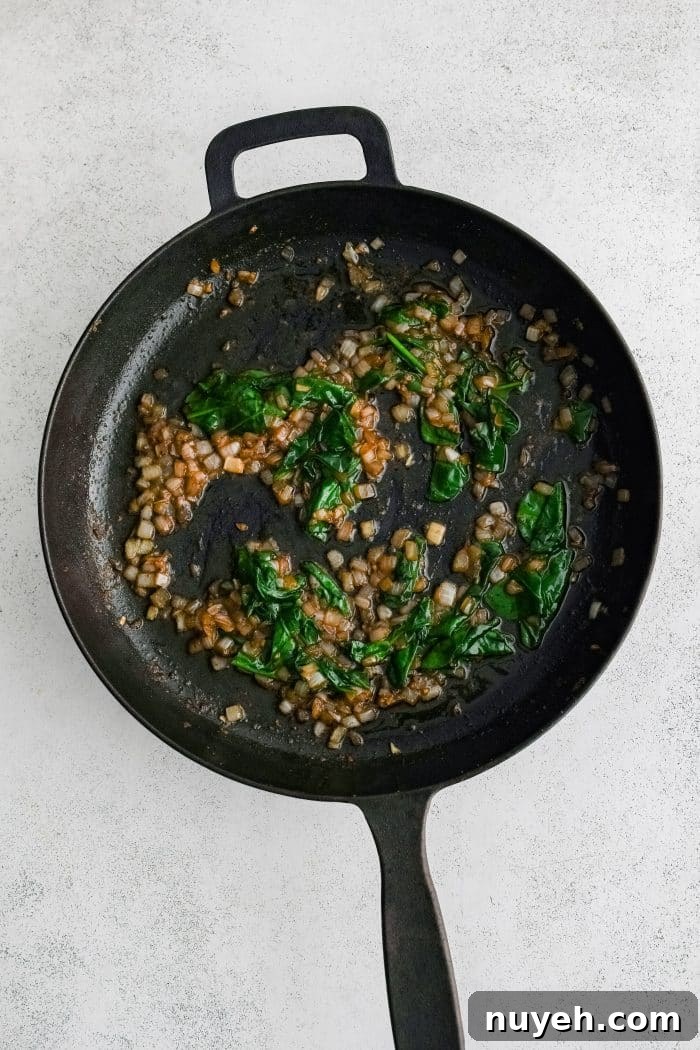 Large cast iron skillet filled with sauteing golden softened onions, garlic, and wilted fresh spinach.