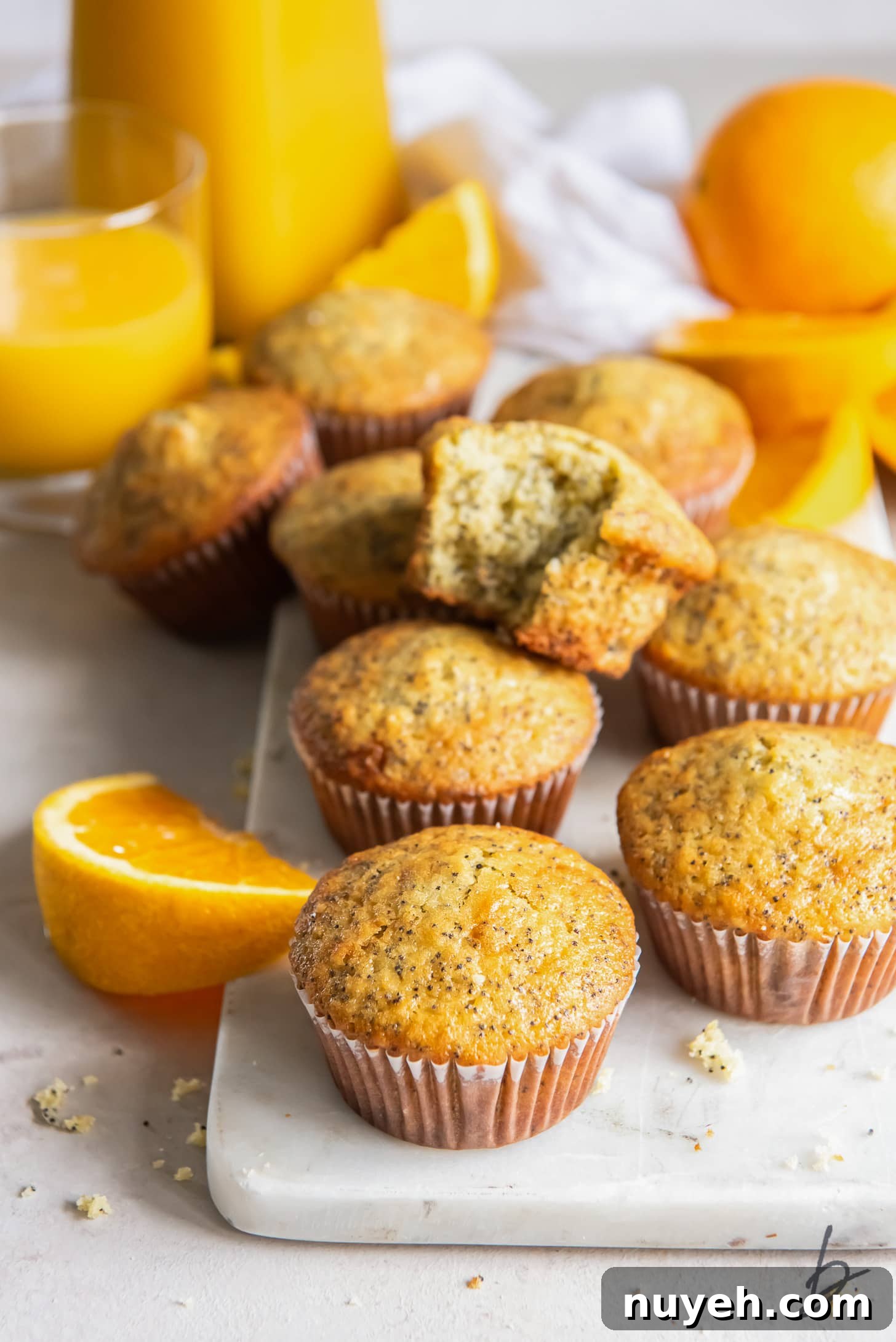 Zesty Orange Poppy Seed Muffins Recipe 2 Orange poppy seed muffins on a marble slab next to oranges and orange slices