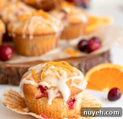 cranberry orange muffin with glaze and orange zest on open paper muffin liner.