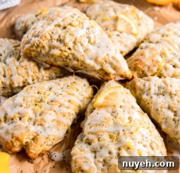 lemon poppyseed scone with glaze on top of more scones on parchment paper.