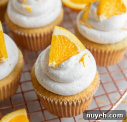 mimosa cupcake with an orange slice as garnish on wire cooling rack.