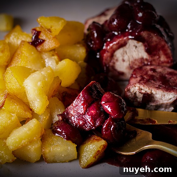 A plate of roast pork with red wine cherry sauce with crispy sautéed potatoes.