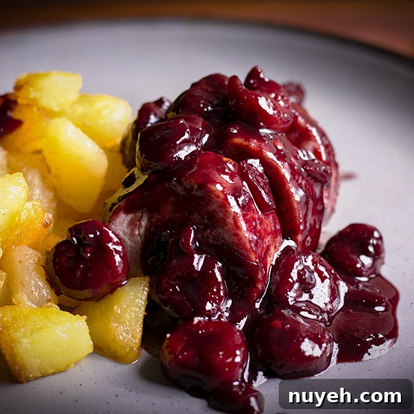 A plate with slices of roasted pork tenderloin with red wine cherry sauce and crispy potatoes.