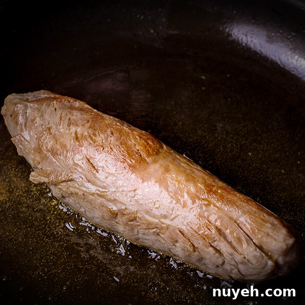 Browning a pork tenderloin in a skillet.