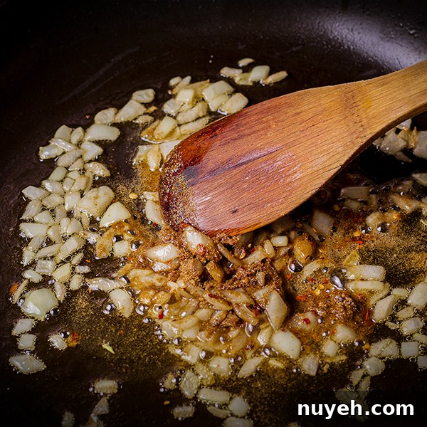 Stirring chopped onions and spices in a skillet.