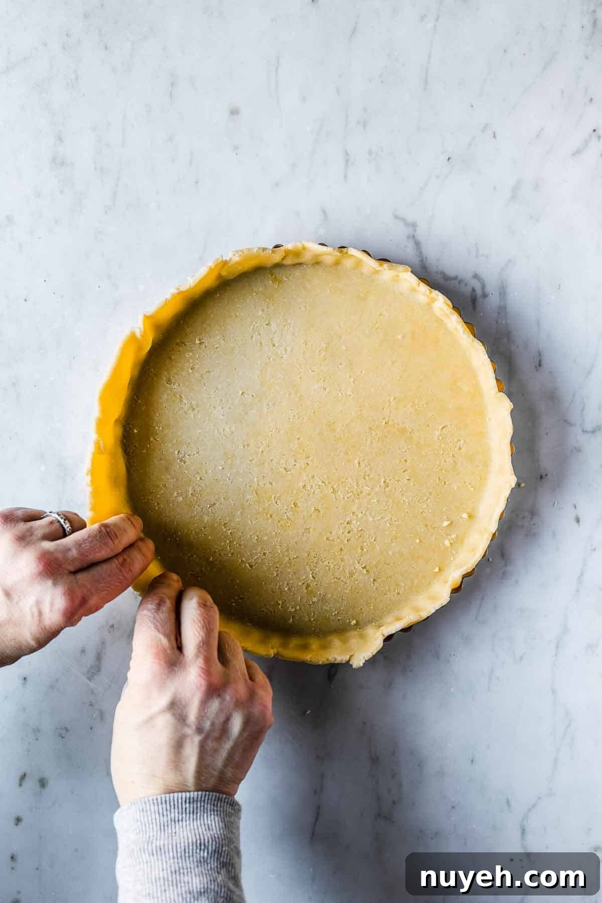 Tart dough being pressed into a fluted tart pan.