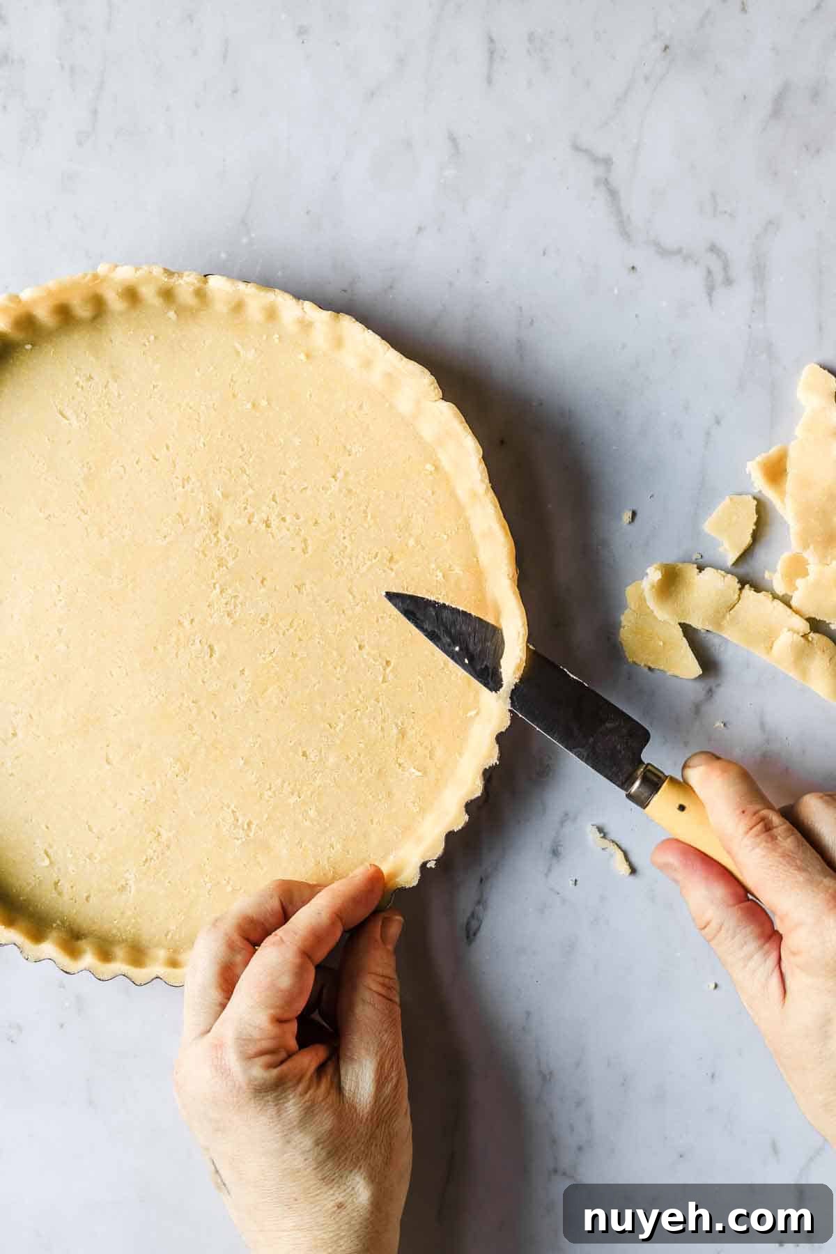 Hands holding a knife and trimming extra dough off tart.
