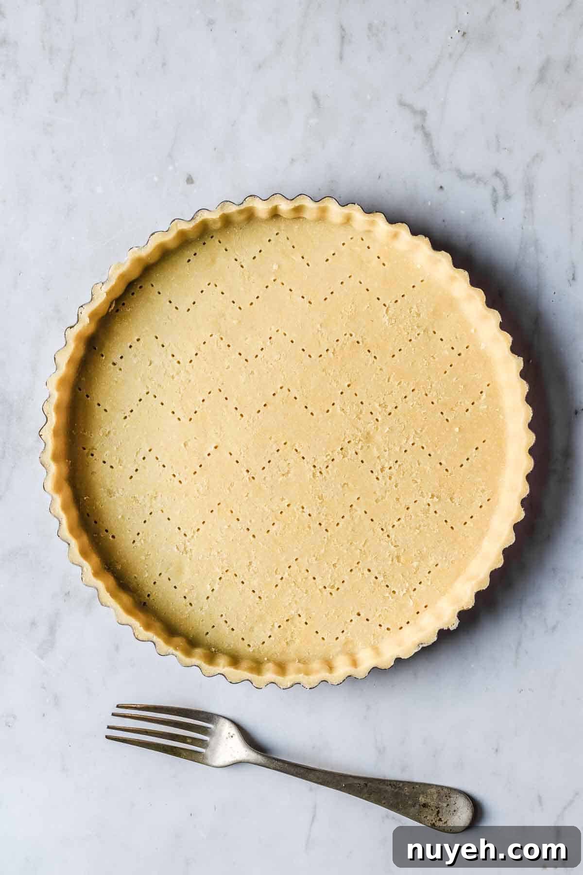 Tart dough in pan that has been docked with a fork in a chevron pattern.