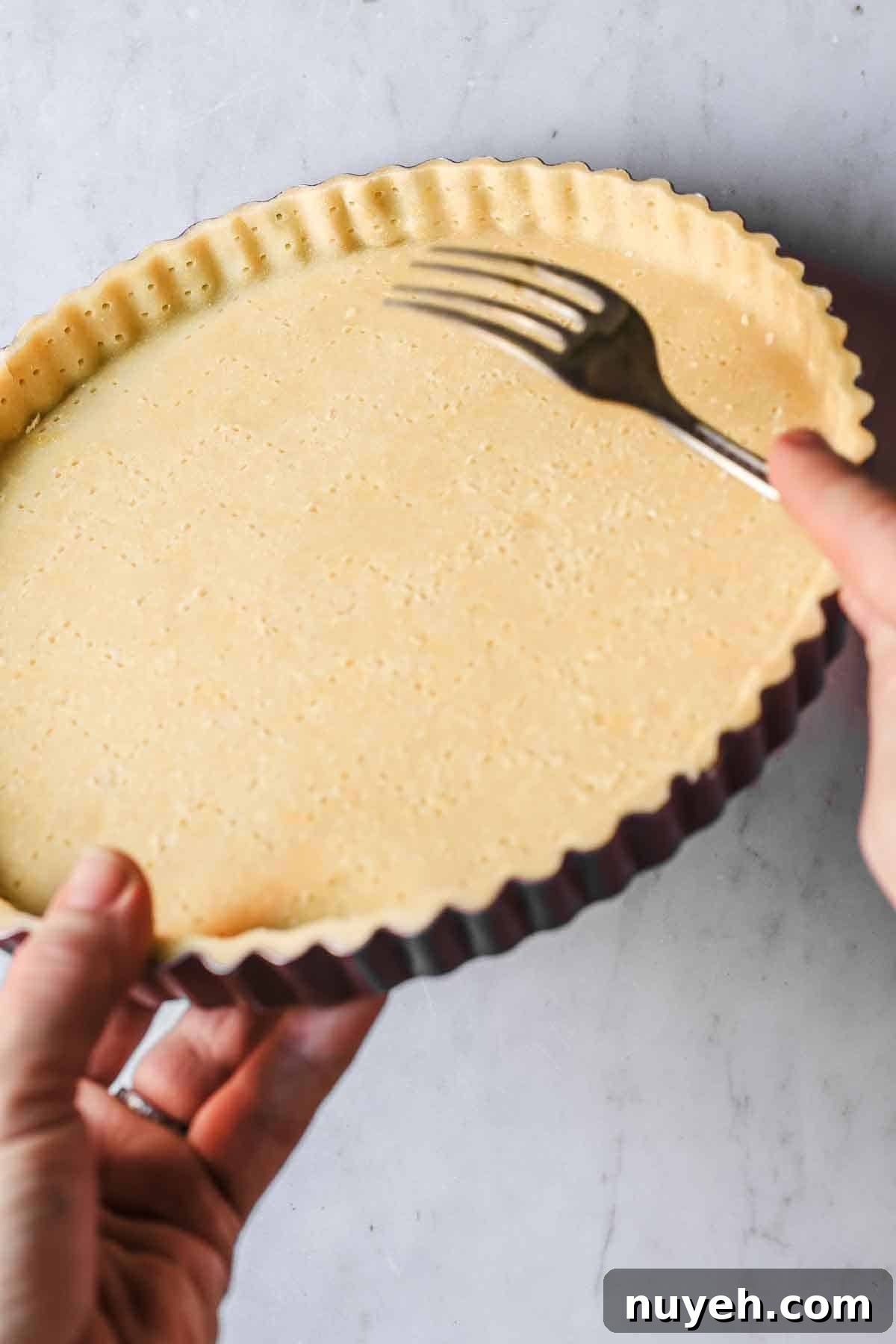 Hands holding a fork to dock sides of tart crust.