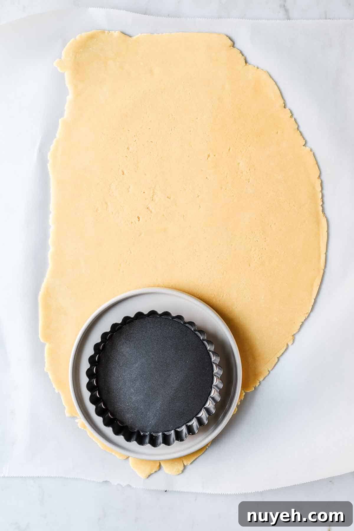 Rolled dough with a plate and small tart pan on top to show size of dough circle needed.