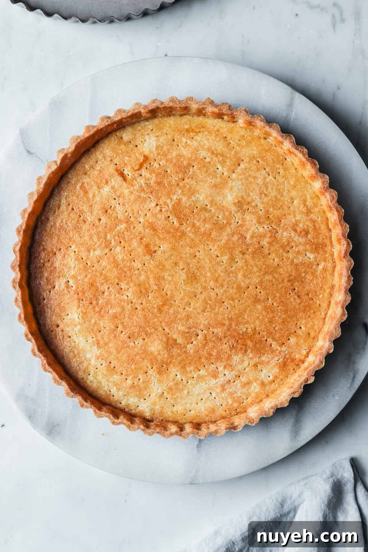 A golden brown baked pate sucree tart shell on a marble platter.