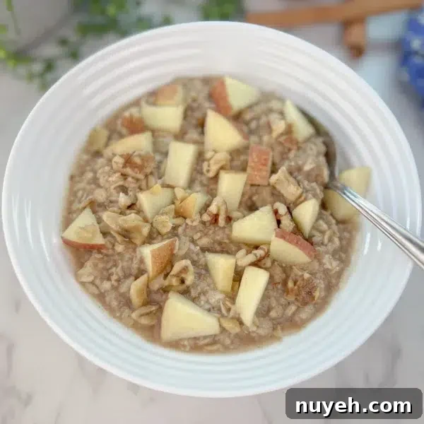 oatmeal in white bowl with fresh apple pieces and walnuts