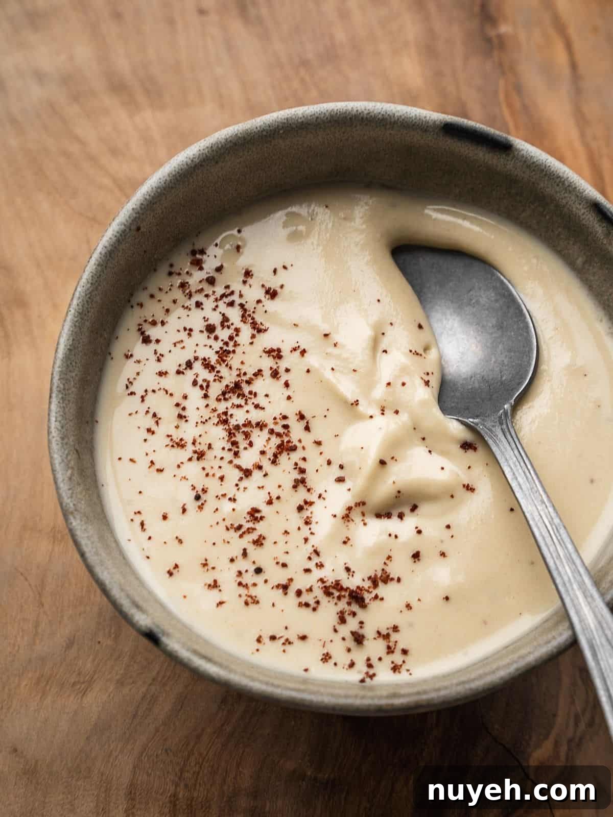 Creamy tahini sauce garnished with sumac in a bowl with a spoon.