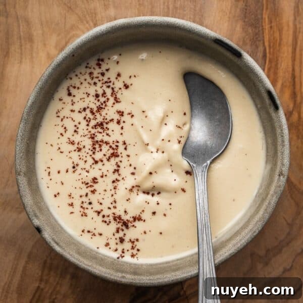Creamy tahini sauce garnished with sumac in a bowl with a spoon.