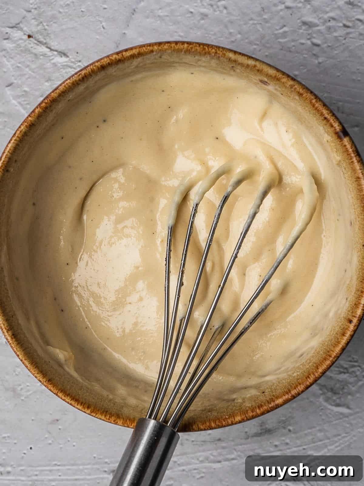Creamy tahini sauce in a bowl with a whisk.