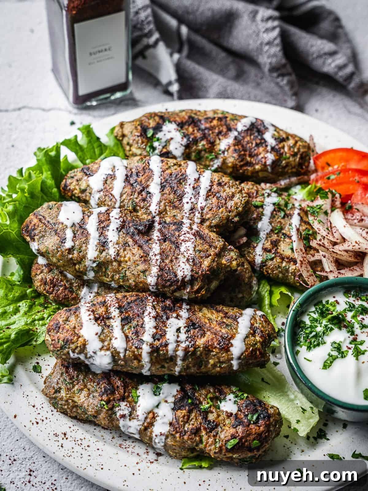 Beef kofta on a plate with a side of vegetables and drizzled with yogurt sauce.