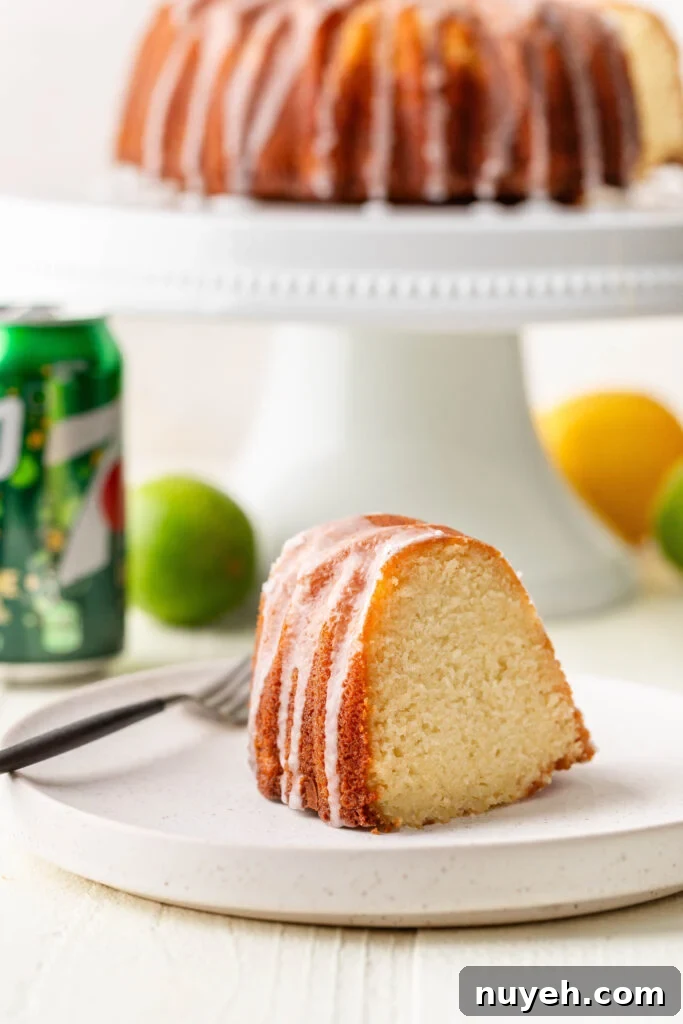 slice of 7-up pound cake on a white plate with a can of 7-up, lemon, lime and whole cake in the background
