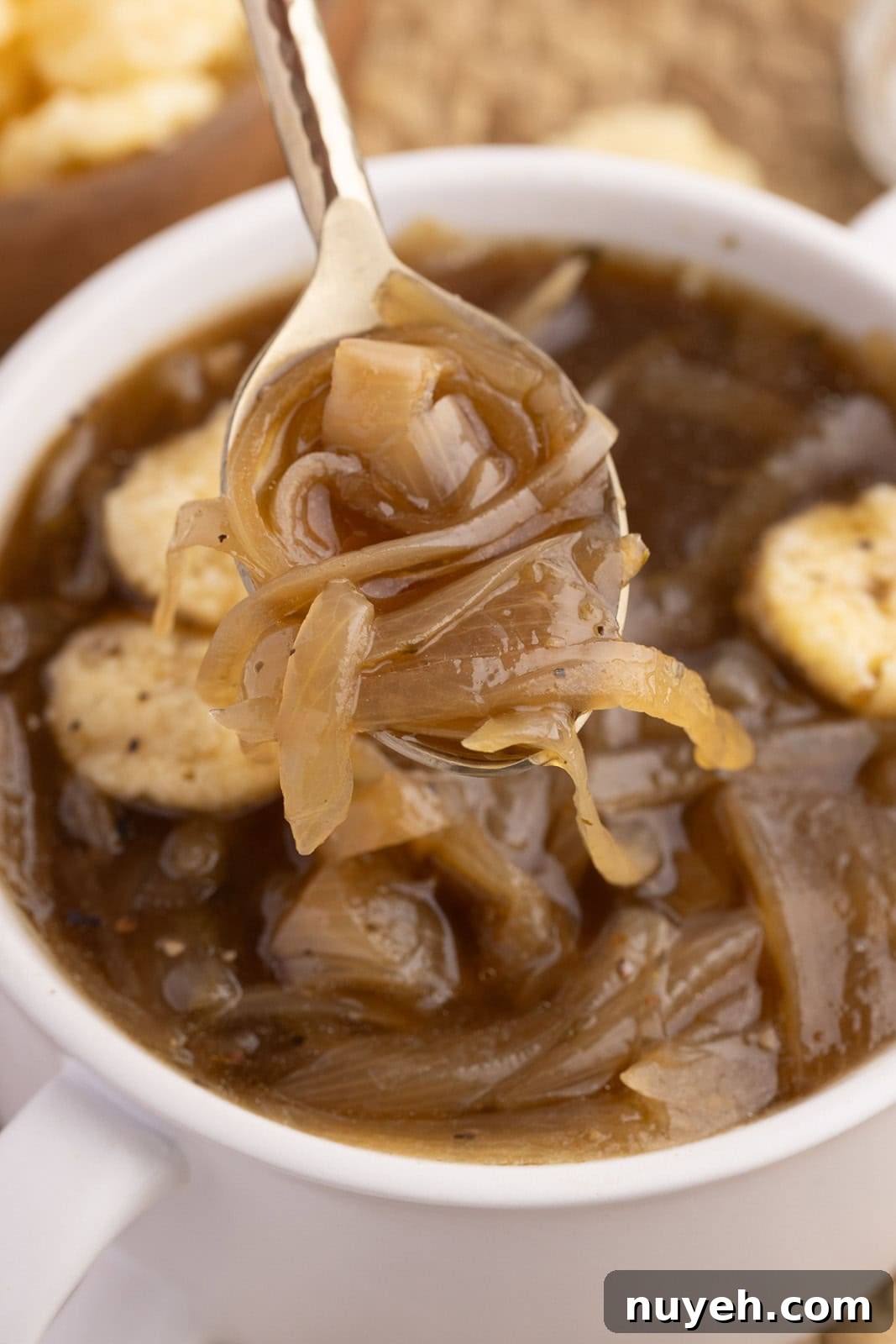 closeup view of white soup cup of onion soup and silver spoon containing soup in forefront