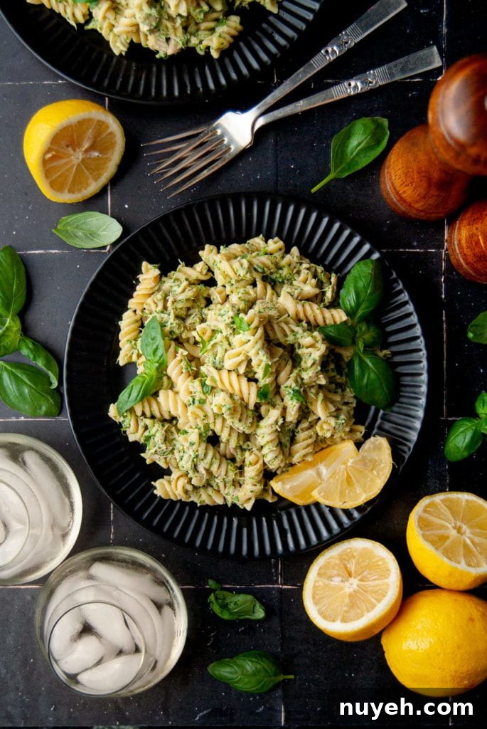 4-Ingredient Canned Tuna and Pesto Pasta Salad 8 serving of tuna pesto pasta on a black plate surrounded by lemon and basil