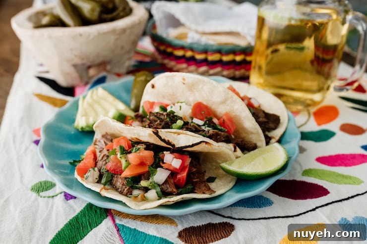 three slow cooker brisket tacos Suadero on a turquoise plate topped with pico de gallo and with a wedge of lime, sliced avocado and escabeche and beer on the side