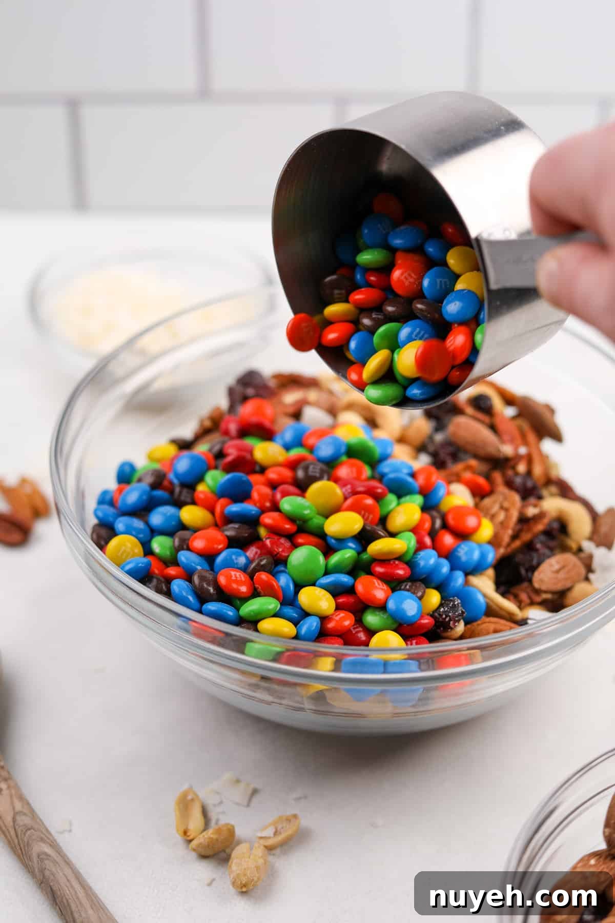 Pouring M&M's into a bowl of mixed nuts.