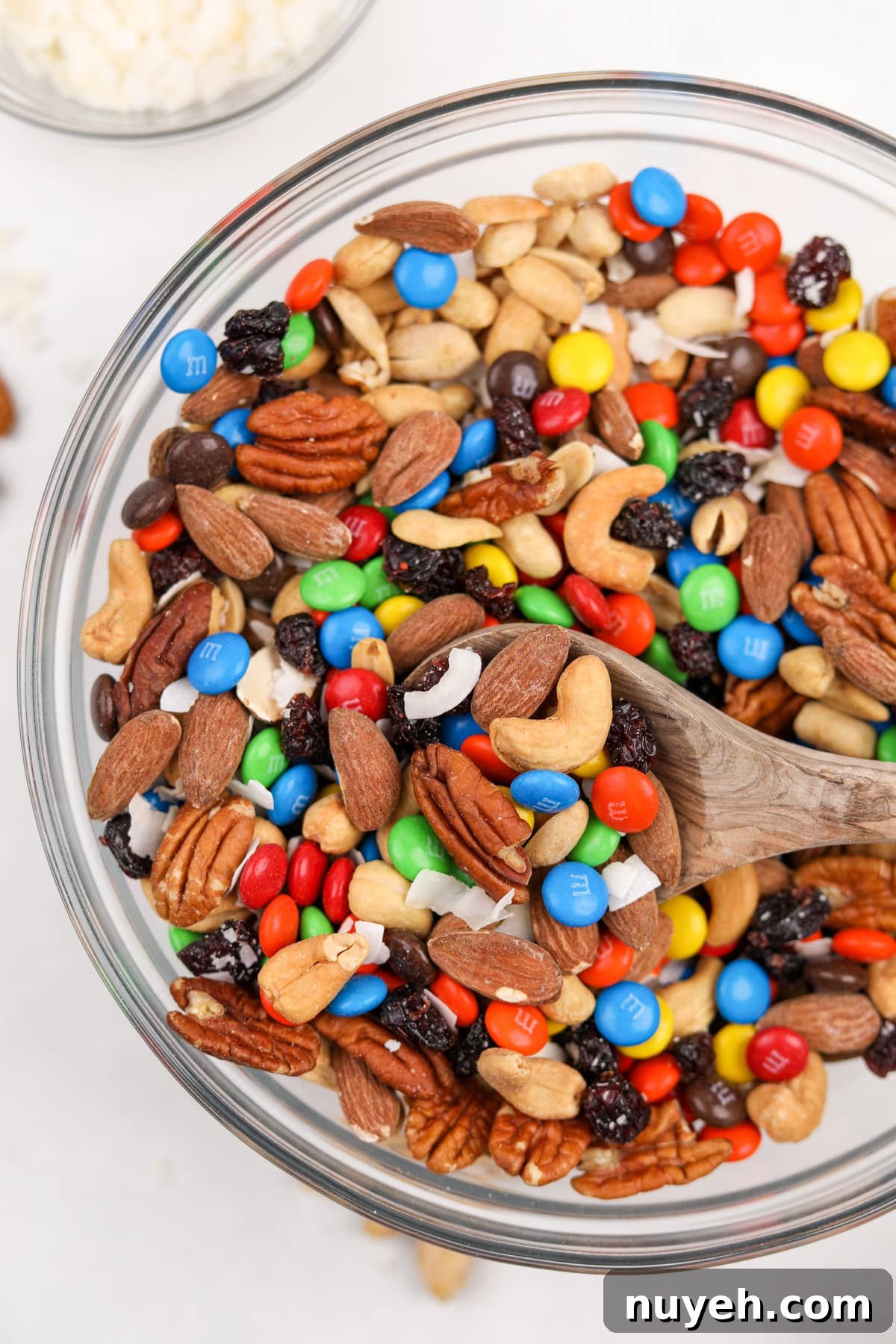 A large bowl of trail mix being scooped with a wooden spoon.