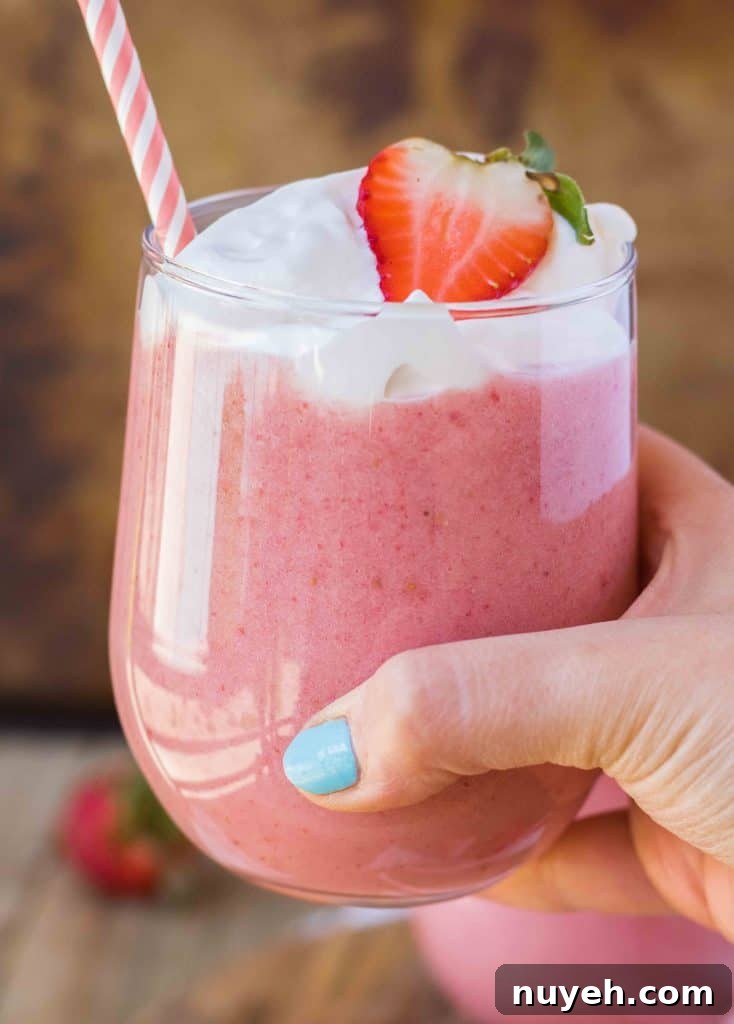 Creamy Strawberry Banana Yogurt Smoothie Recipe 2 Hand holding a strawberry banana smoothie with whipped cream and a strawberry on top.