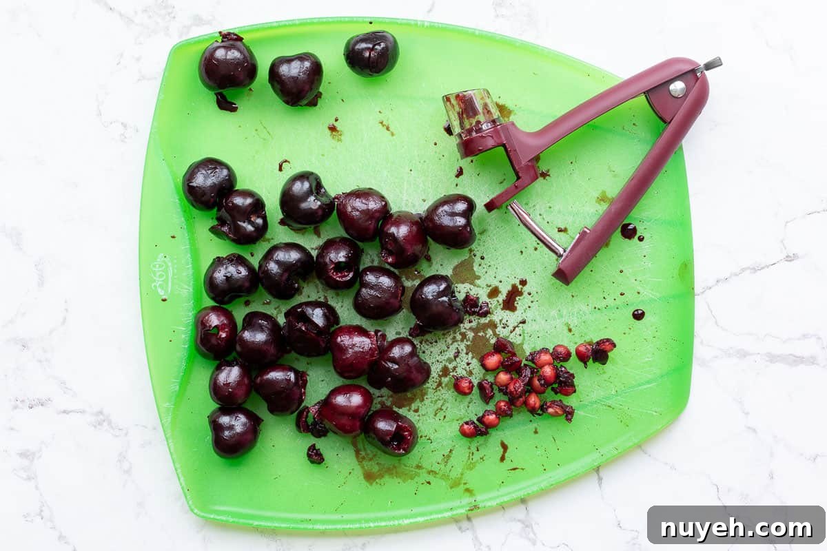 pitted cherries on cutting board with cherry pitter and cherry pits.