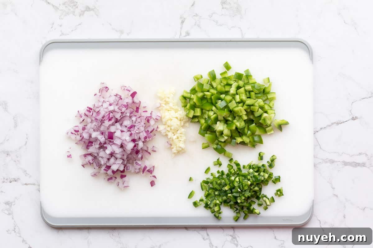 chopped red onion, minced garlic, chopped bell pepper, and chopped jalapeno pepper on cutting board.